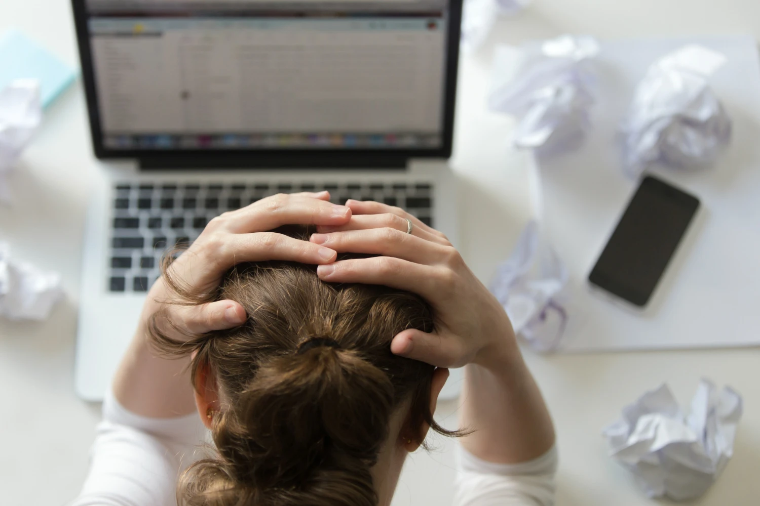 Imagem que ilustra como evitar o burnout em profissões criativas. Mostra uma pessoa estressada, com as mãos na cabeça, rodeada de anotações amassadas e um computador.