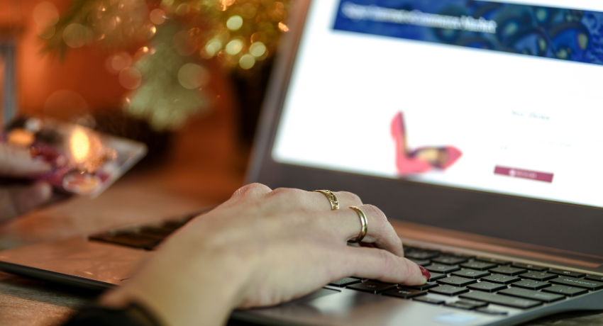 Mão digitando em laptop enquanto segura cartão de crédito, representando pagamento ou compra em loja online.